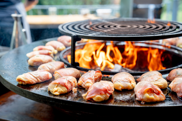 Hähnchen im Speckmantel auf dem Grill am offenen Feuer